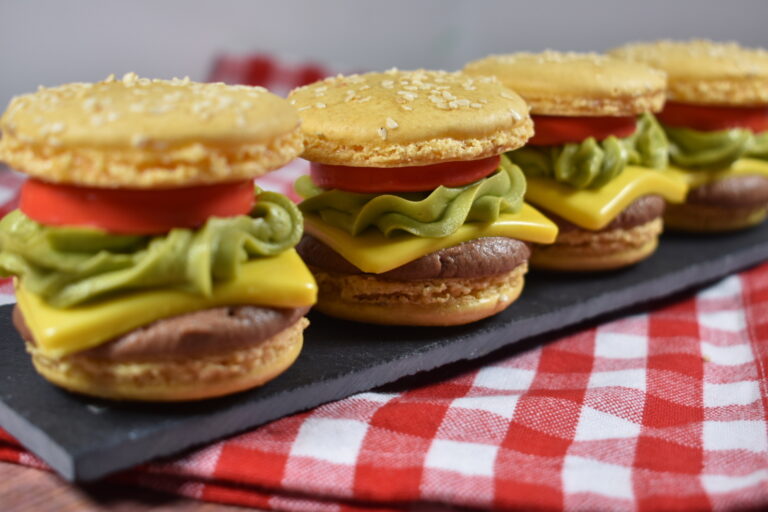 Four cheeseburger macarons arranged on a slate board