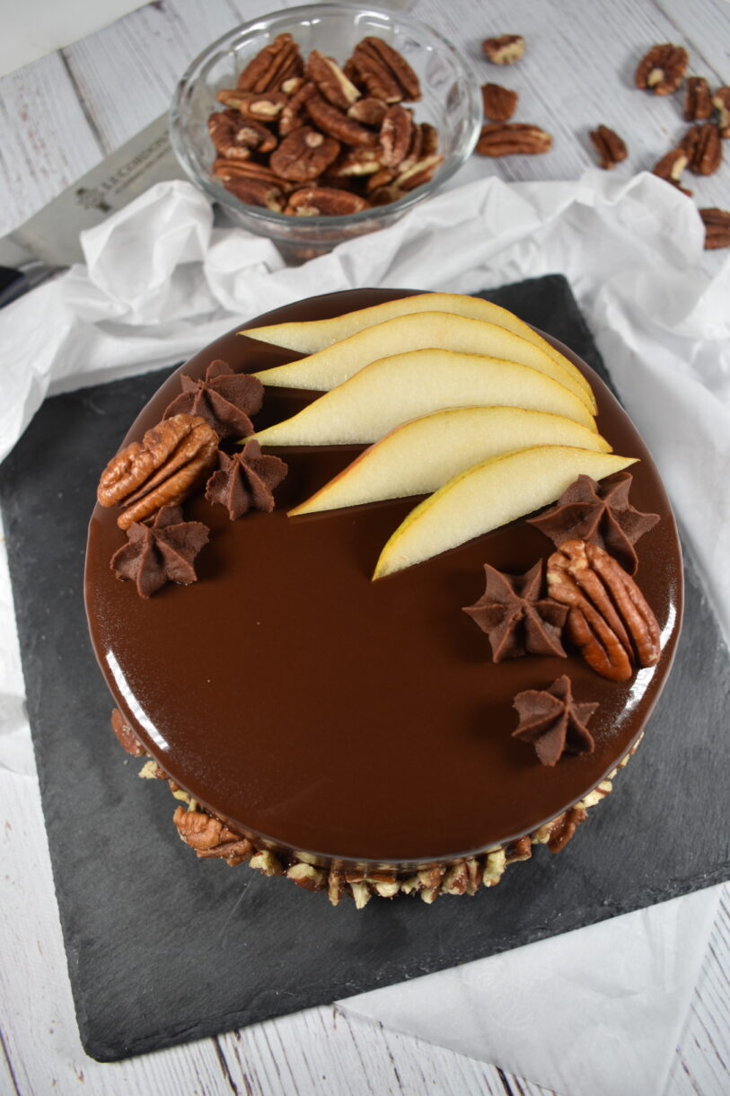 Autumn pear entremet with chocolate mirror glaze, sliced pears, pecans, and chocolate ganache, on a slate board