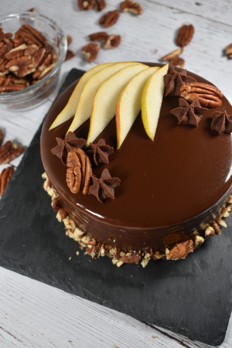Autumn pear mousse cake on a slate board, next to a glass bowl of pecans