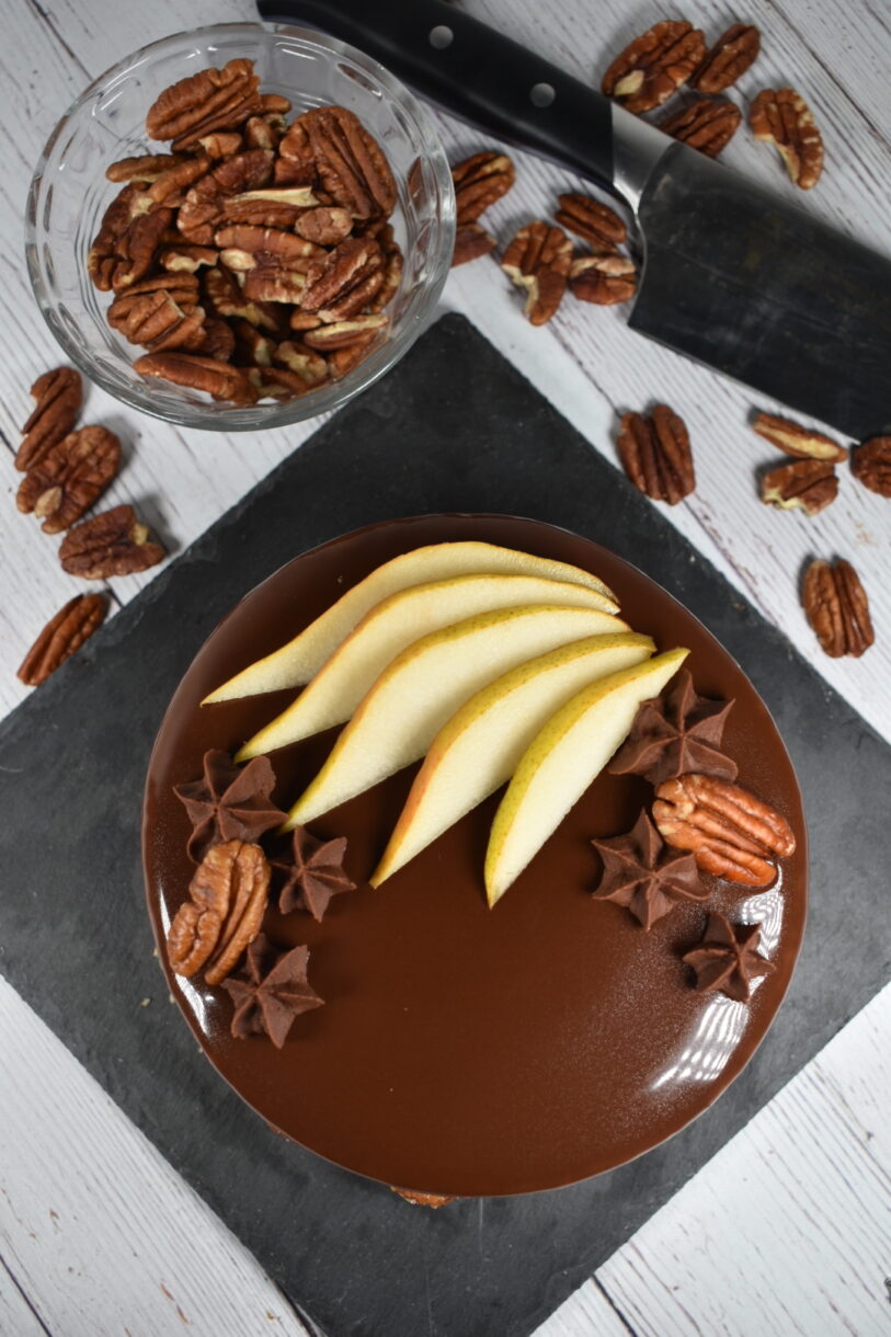Autumn pear entremet on a slate board, surrounded by a bowl of pecans and a chef's knife