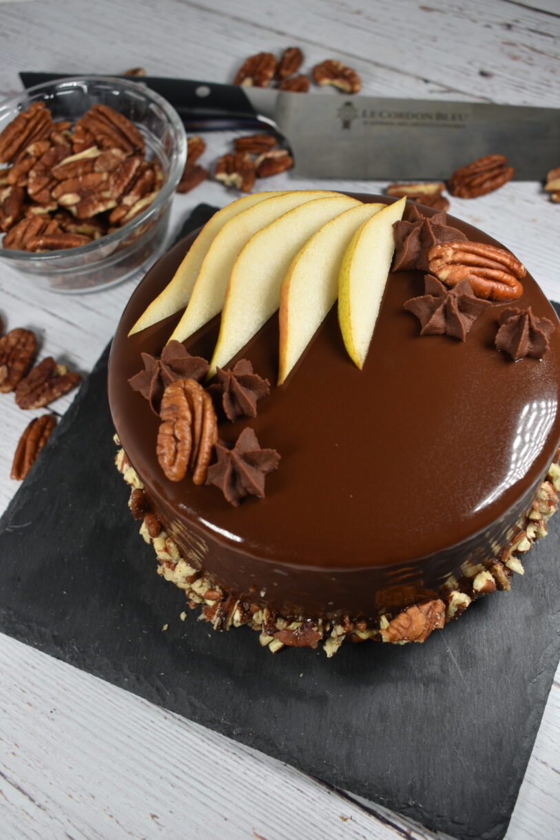 Autumn pear entremet with shiny mirror glaze, surrounded by pecans and a chef's knife