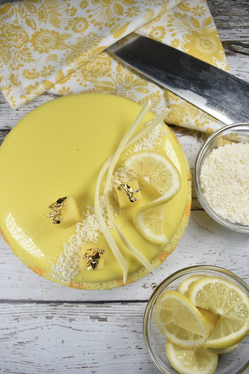 Mango, lemon and white chocolate entremet with a yellow tea towel, knife, bowl of lemons and bowl of coconut