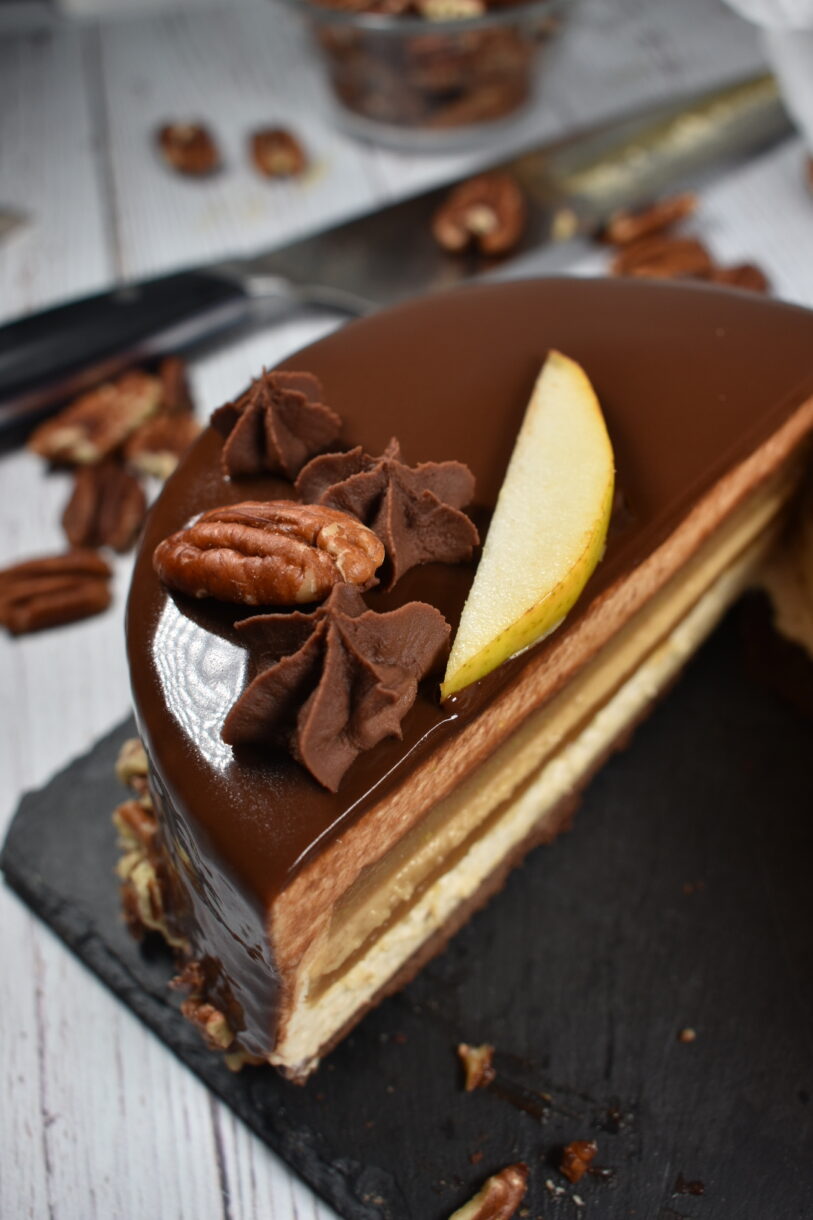 Chocolate and pear entremet cake on a slate board, surrounded by pecans and a chef's knife