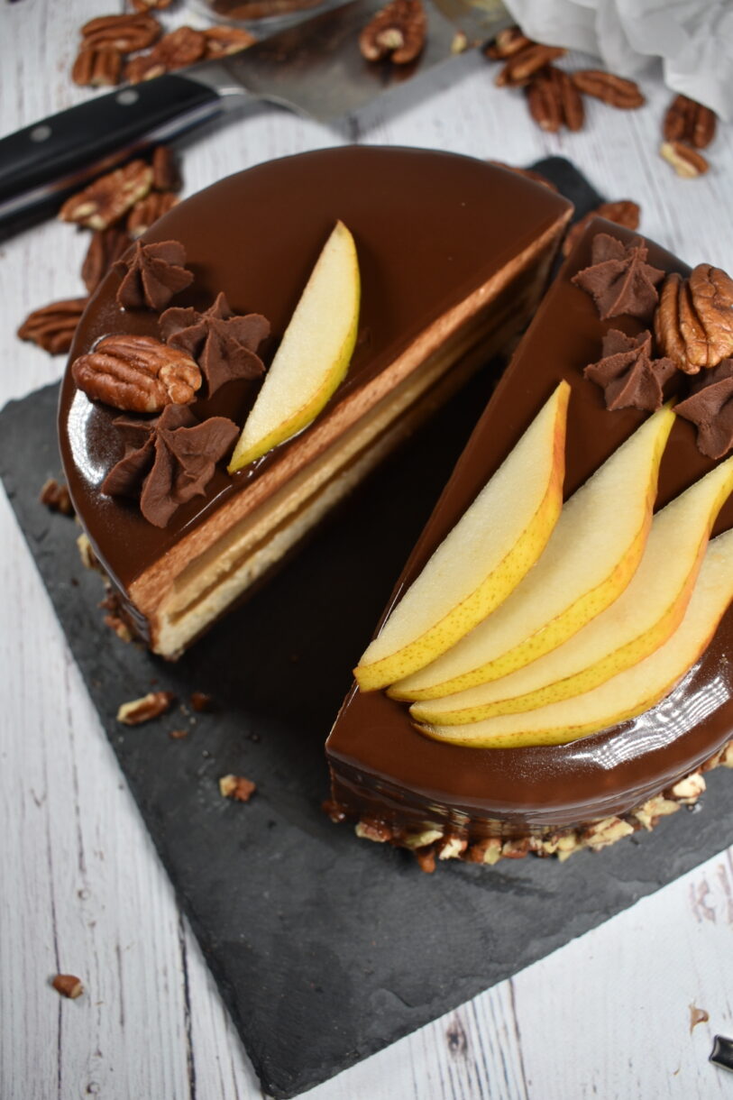 Slice autumn pear entremet on a slate board, surrounded by pecans and a chef's knife