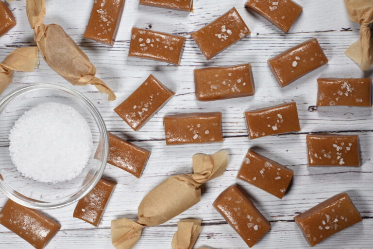 Cider caramels and a bowl of salt on a white wooden surface