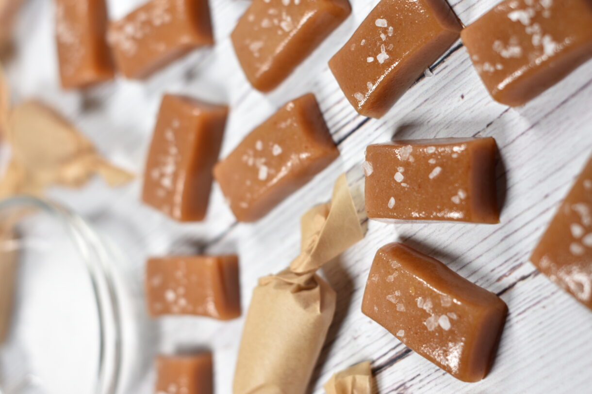 Wrapped and unwrapped cider caramels and a bowl of sea salt on a wooden surface