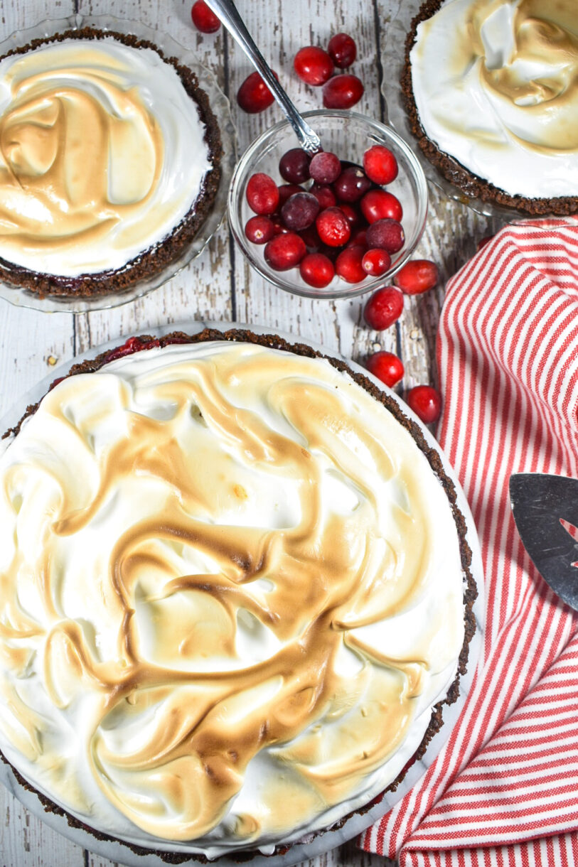 Cranberry-orange meringue pie, white surface, bowl of cranberries, and a red and white tea towel