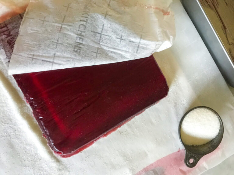 Peeling away parchment from slab of cranberry jelly candy