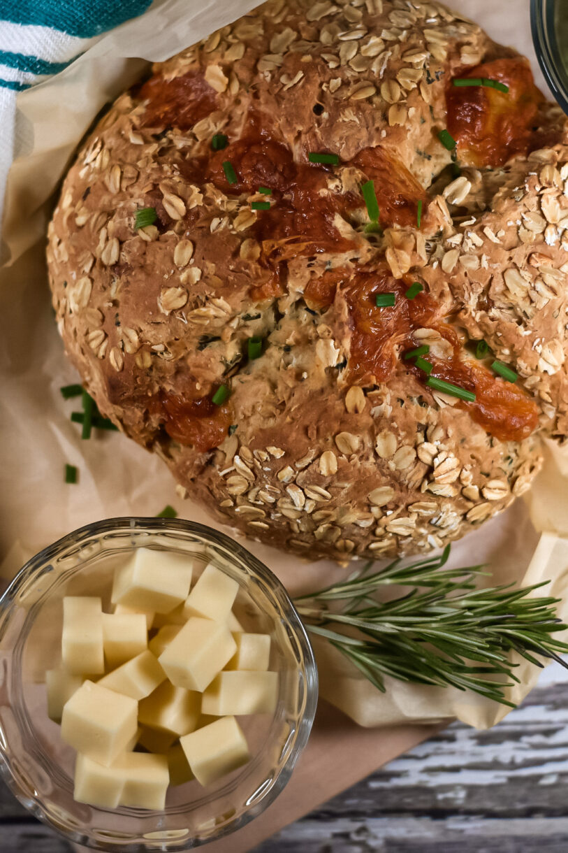 a loaf of soda bread garnished with chives, sitting on a sheet of baking parchment