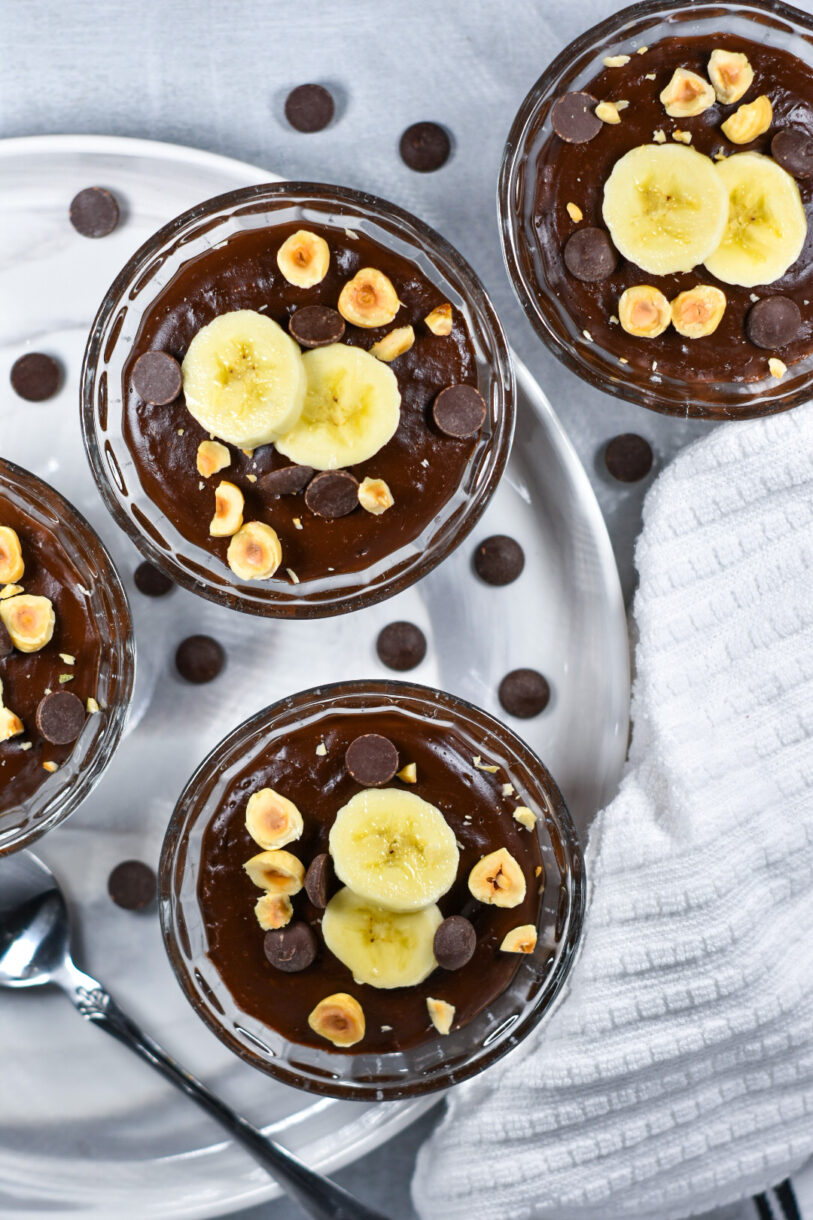 Glass bowls of chocolate pudding garnished with peanuts, bananas, and chocolate chips