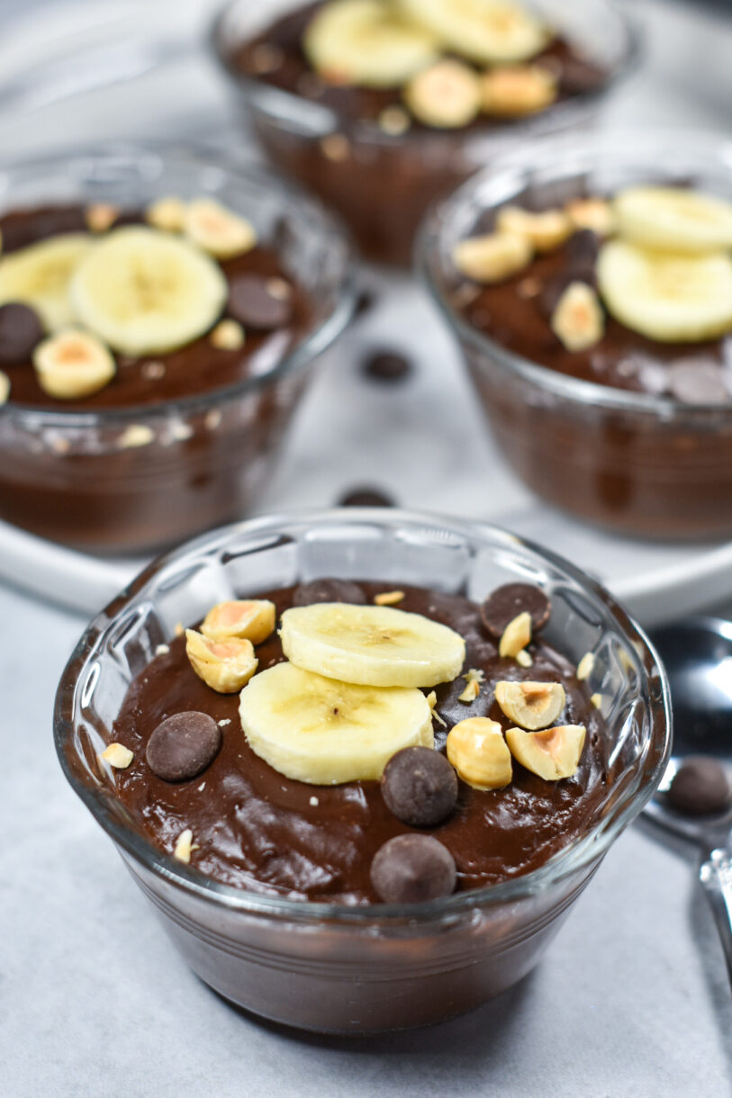 Chocolate Almond Milk Pudding in a glass bowl, garnished with bananas, nuts and chocolate chips