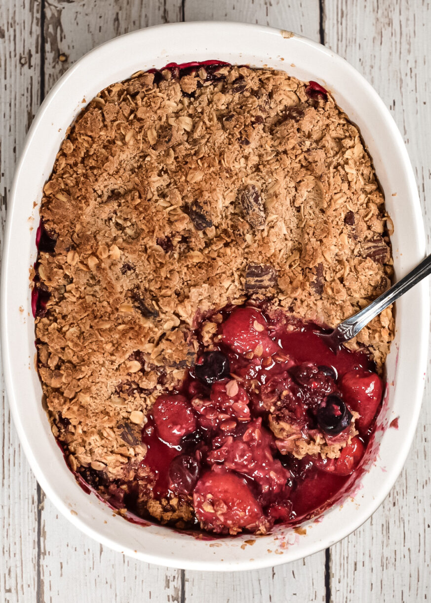 Vegan Mixed Berry Crumble with a spoon, on a white wooden background