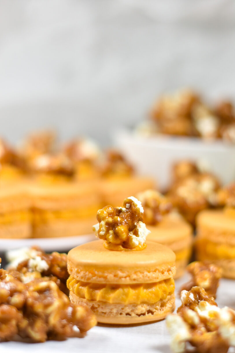 A closeup shot of a caramel macaron with a piece of caramel popcorn on top