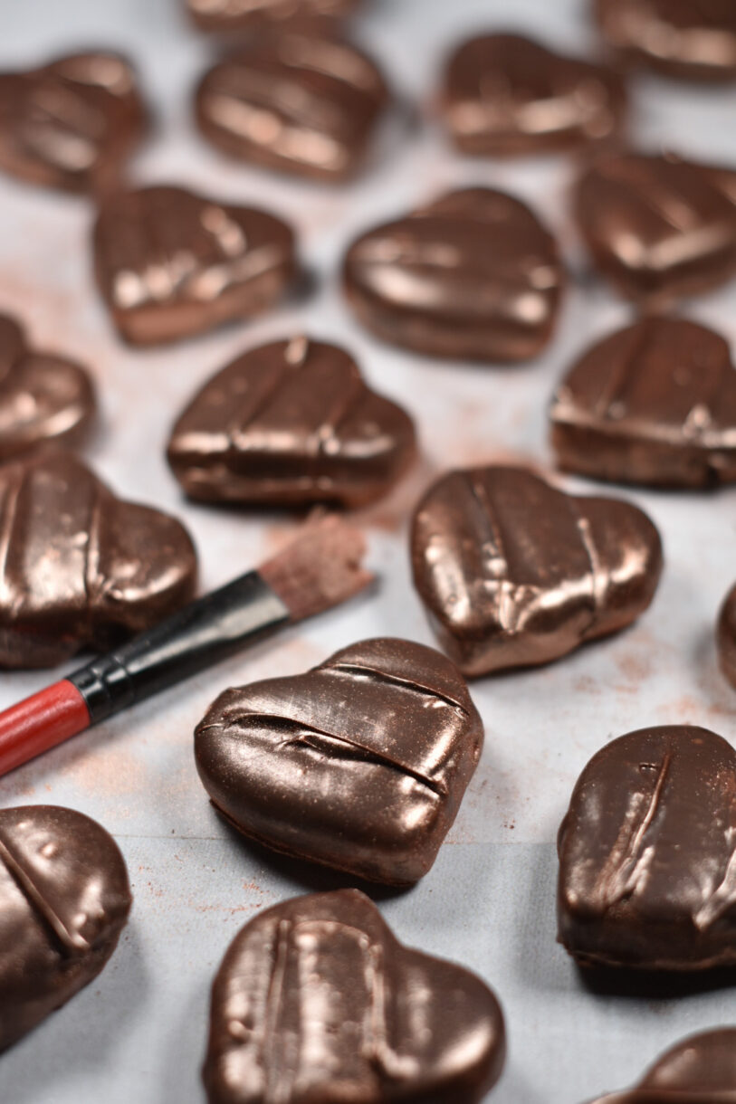 Heart shaped chocolates and a paintbrush with gold lustre dust, on a white background