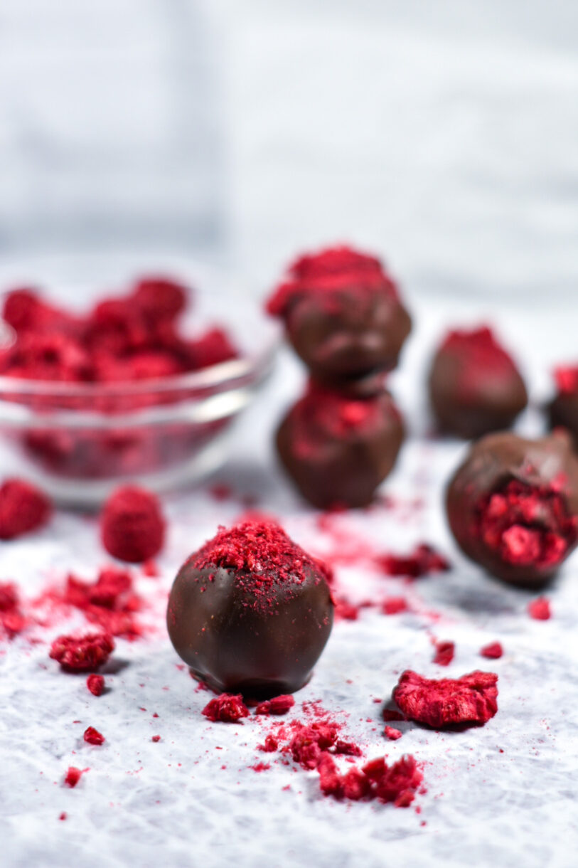 Dark chocolate raspberry truffles and a bowl of crushed dried raspberries on a white surface