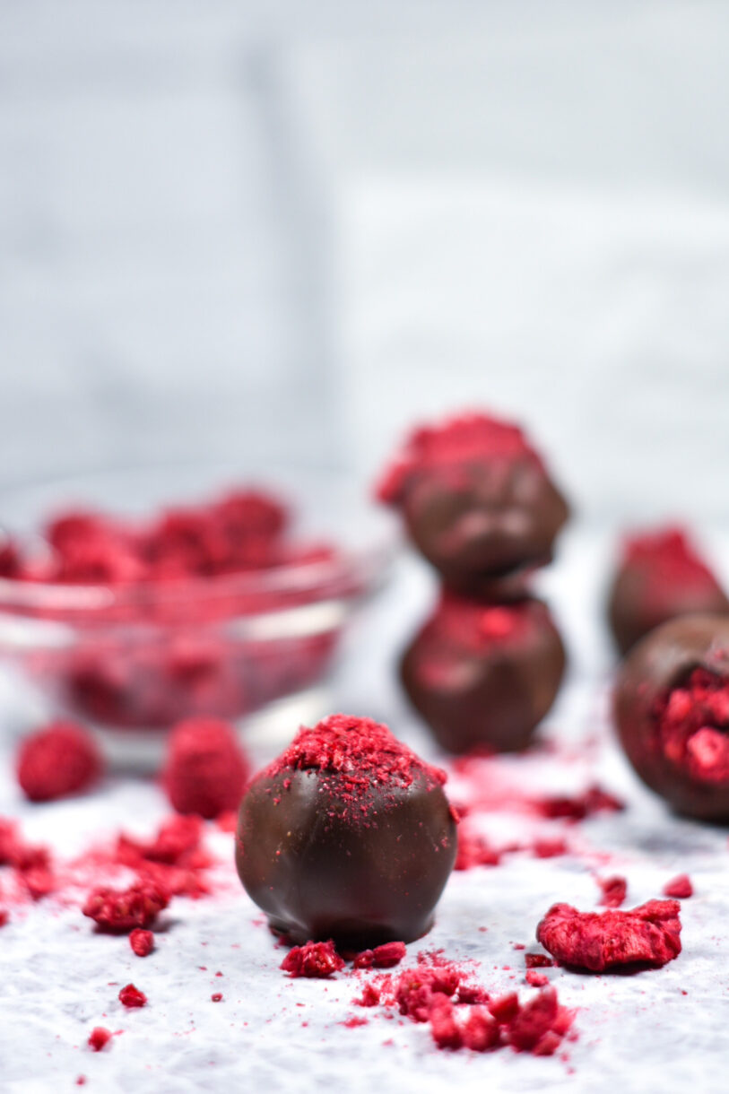 Raspberry truffles and crushed dried raspberries on a white surface