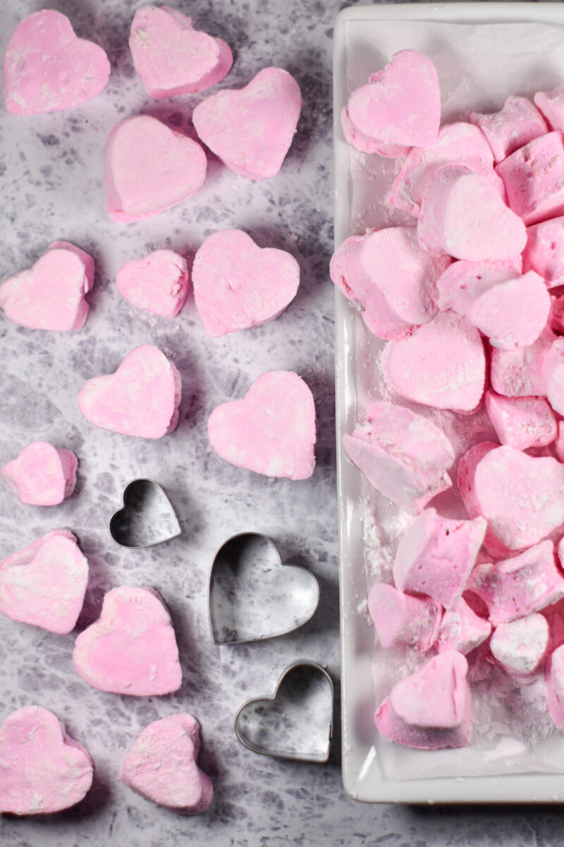 Heart shaped strawberry marshmallows and heart cookie cutters on a grey textured surface