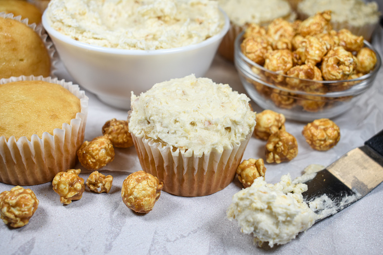a cupcake frosted with caramel popcorn buttercream surrounded by pieces of caramel popcorn
