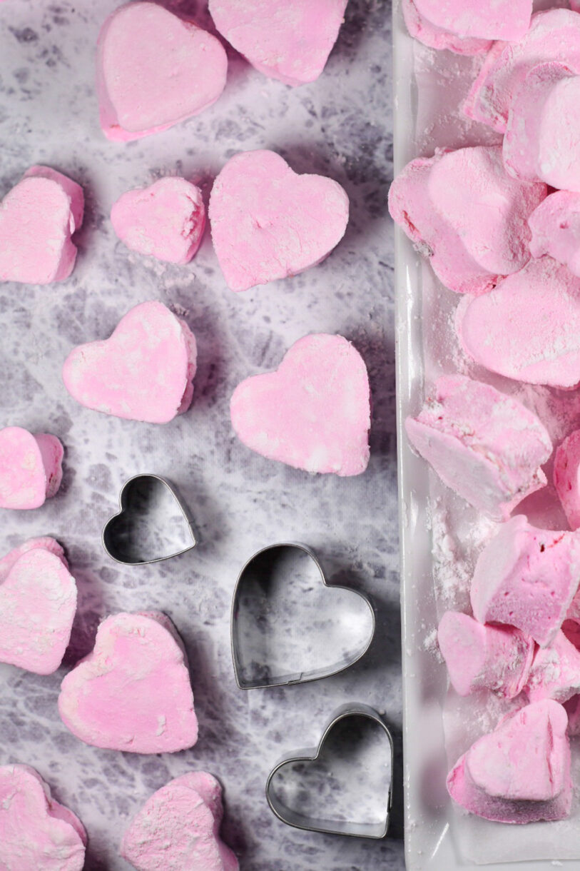 Homemade pink heart marshmallows and three heart cookie cutters on a textured photography backdrop