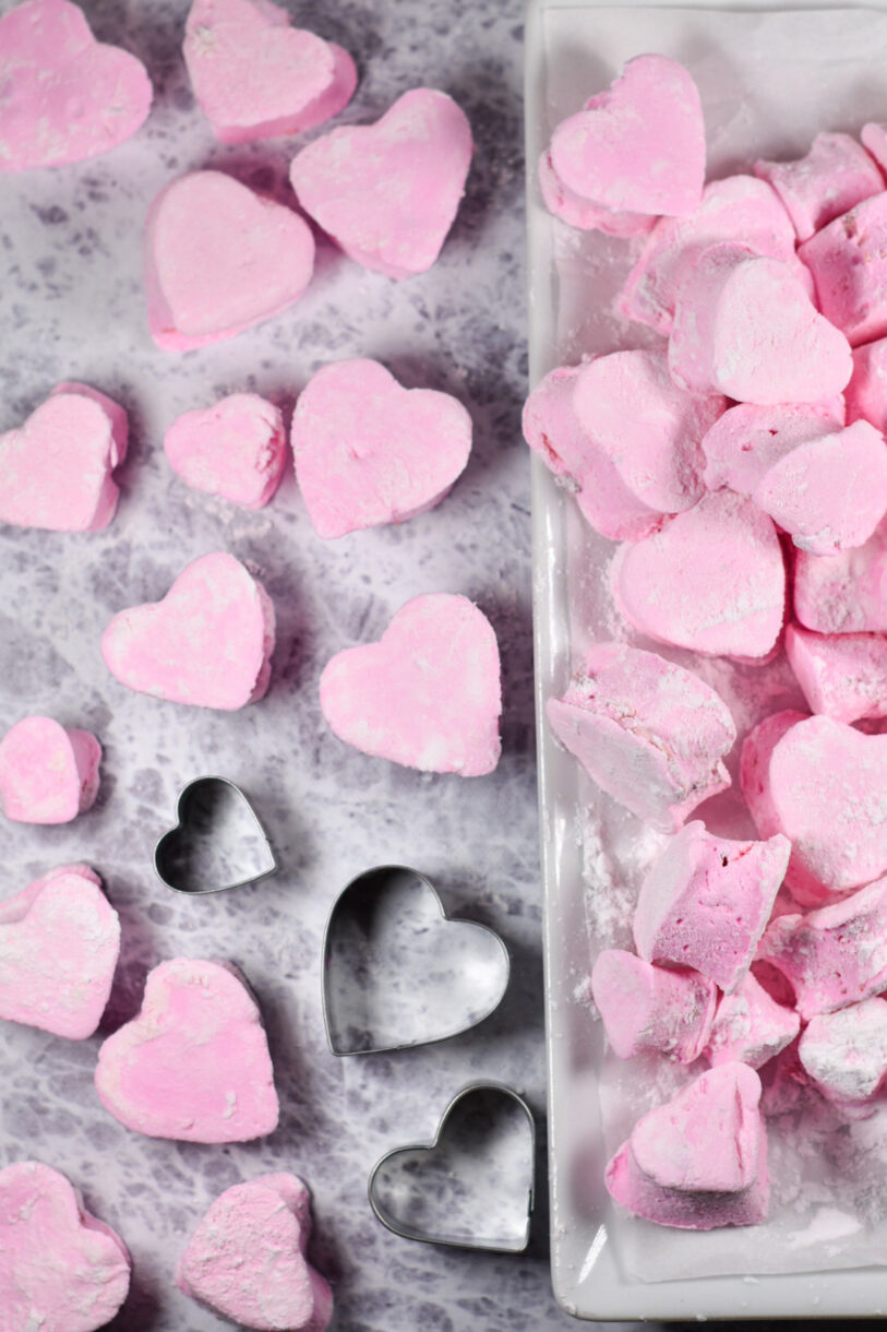 Homemade pink strawberry marshmallows scattered on a grey surface