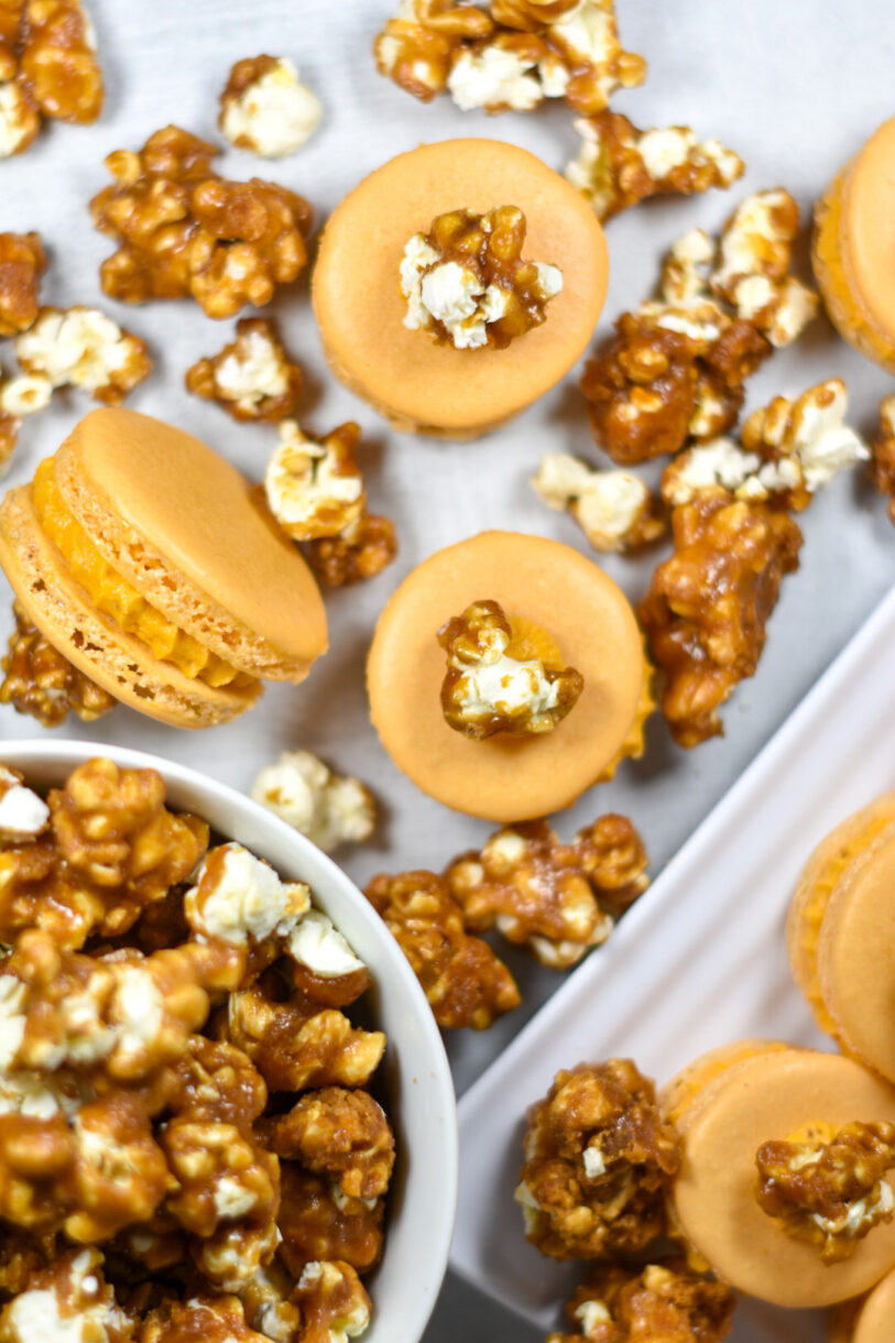 Caramel popcorn buttercream macarons and a bowl of popcorn on a white surface