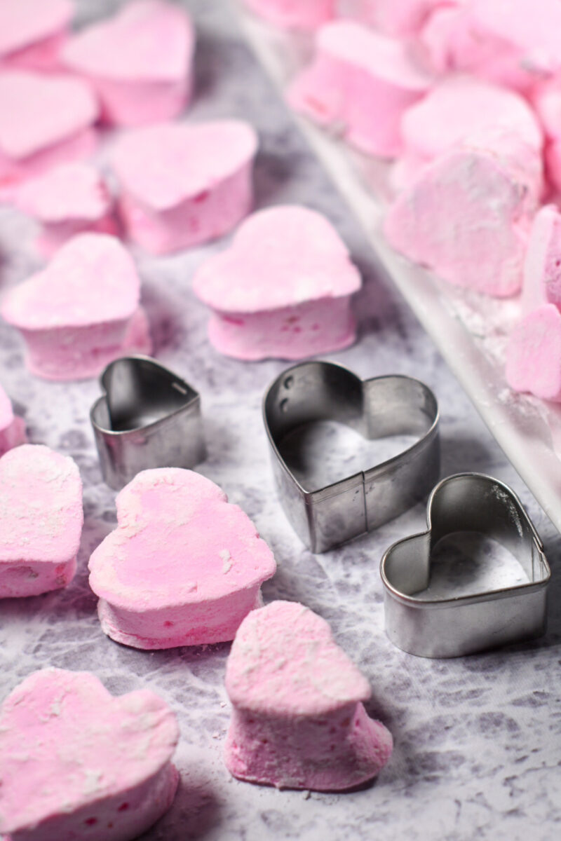 Three metal heart shaped cookie cutters surrounded by pink marshmallow hearts