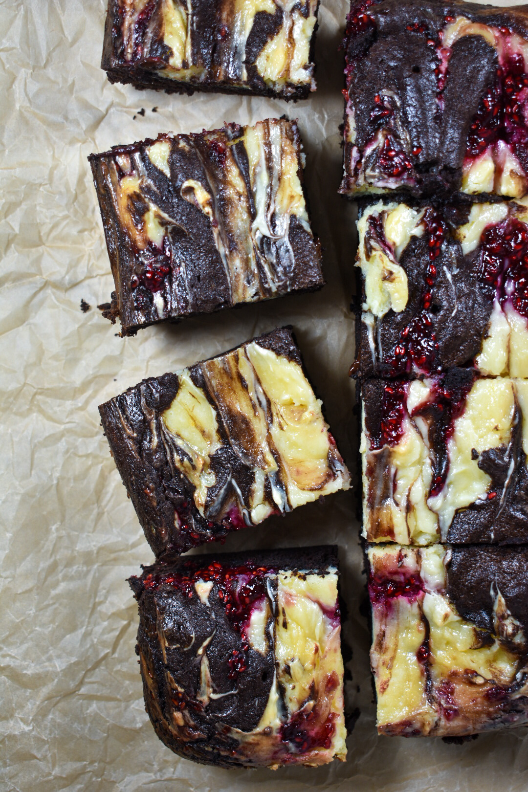raspberry cheesecake brownies on a sheet of brown parchment