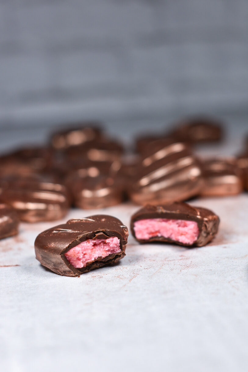 A pair of pink peppermint patties with chocolate coating, on a white surface
