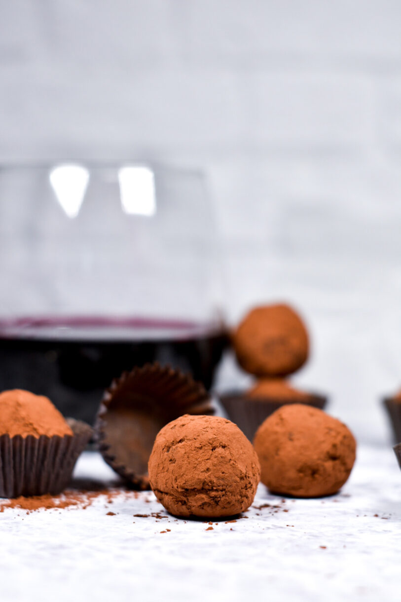Glass of red wine with chocolate truffles, cocoa powder, and truffle cups on a white background