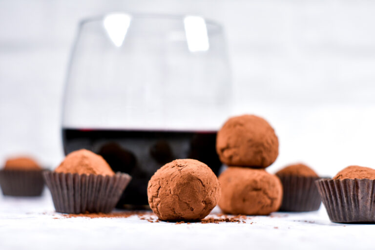 Stack of cocoa powder covered chocolate truffles, with a glass of red wine in the background