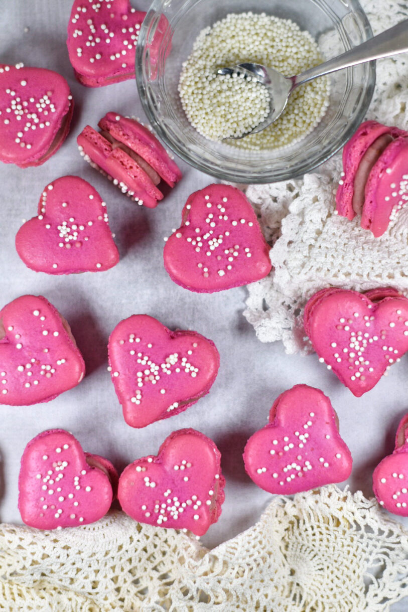 Heart macarons filled with ganache, along with a bowl of white sprinkles