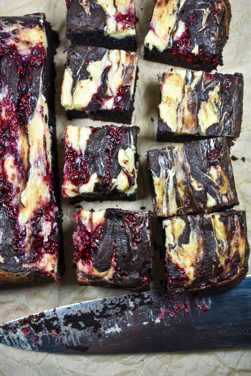 Raspberry cheesecake brownies and a knife on a sheet of parchment