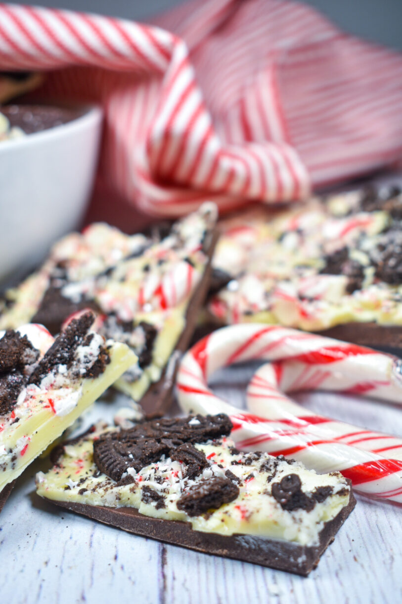 Peppermint bark and candy canes arranged on a white surface with a striped tea towel