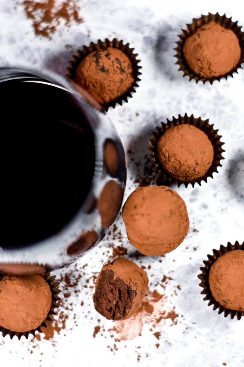 Looking down at a glass of red wine and truffles in truffle cups, on a textured white background