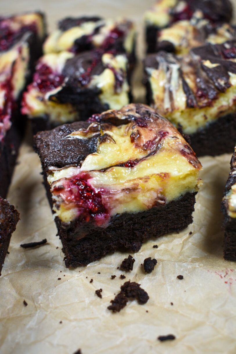 Raspberry cheesecake brownies cut into squares, on a sheet of parchment