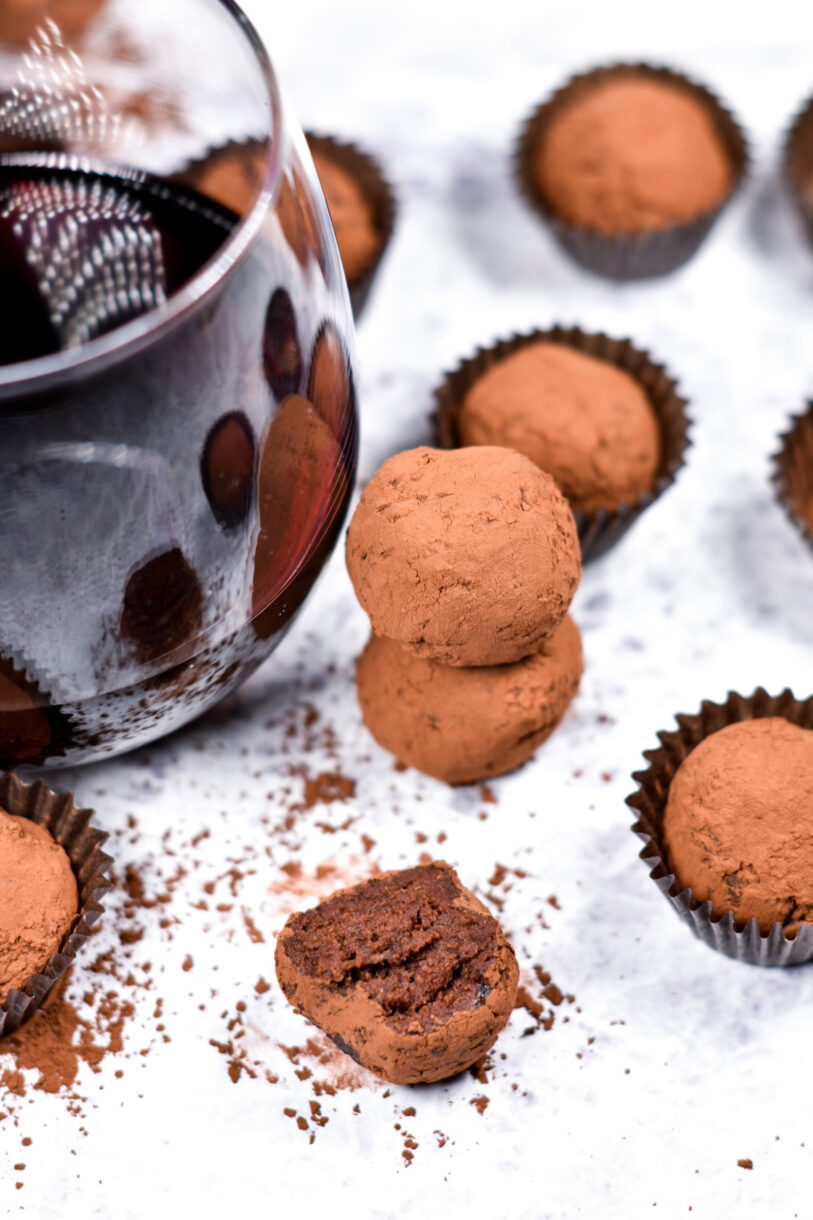 Wine glass and red wine truffles on a white background, with one truffle missing a bite