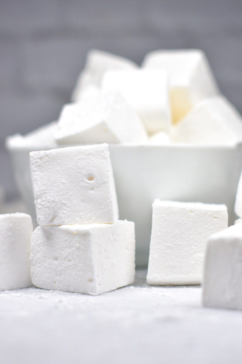 Vanilla bean marshmallows on a white background, with a bowl of marshmallows in the rear