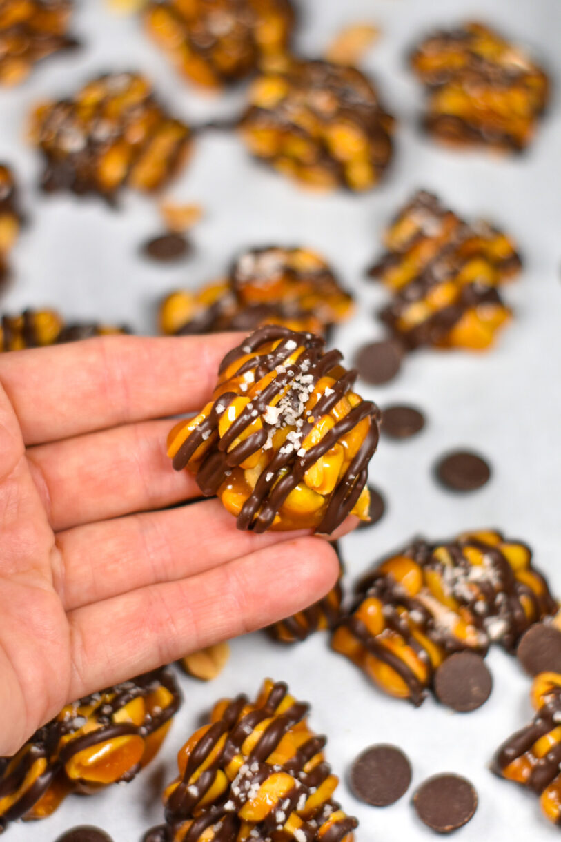 Hand holding a homemade peanut cluster drizzled in chocolate and sprinkled with sea salt