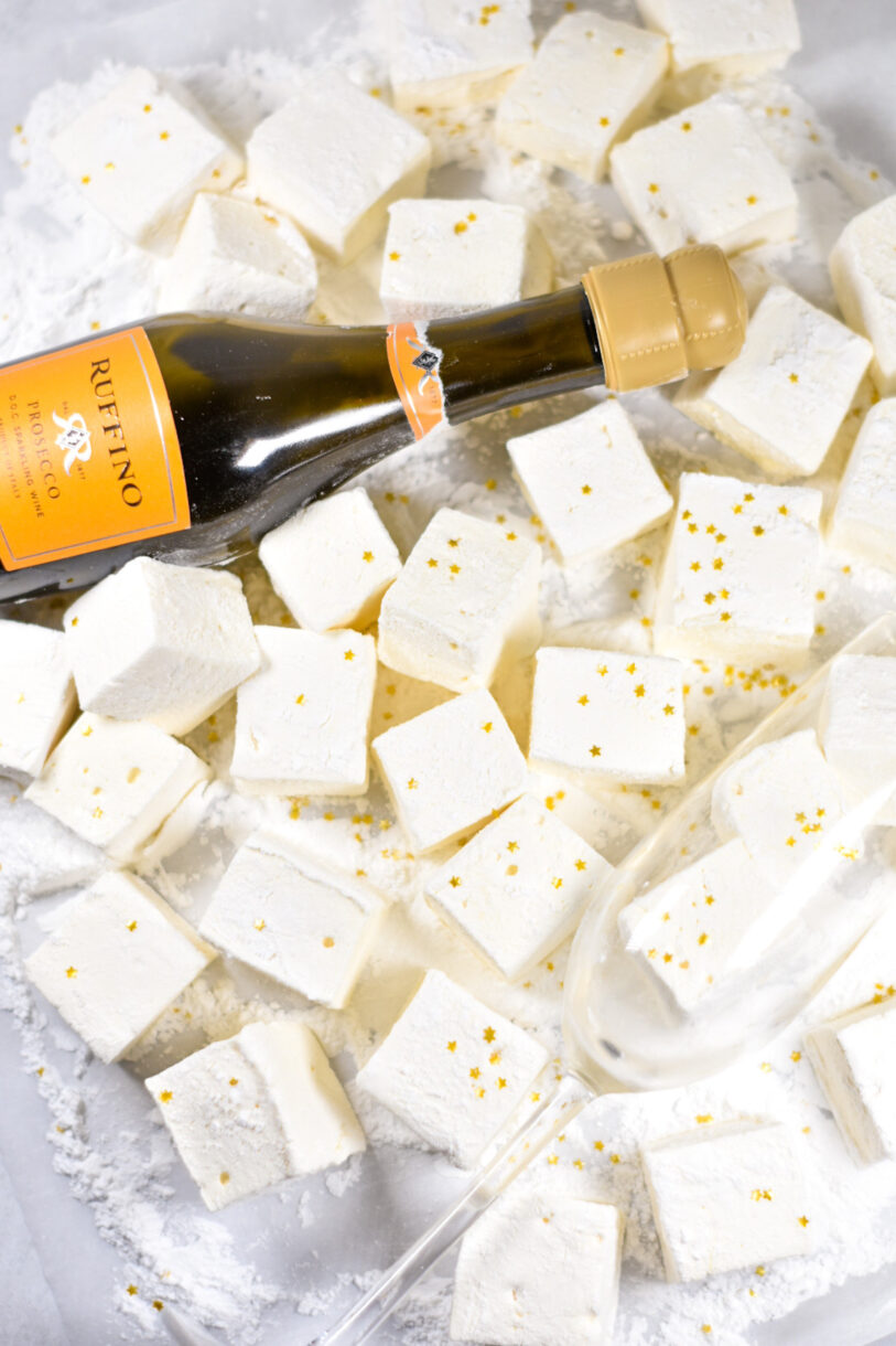 A bottle of sparkling wine, a champagne glass, and marshmallows on a white background