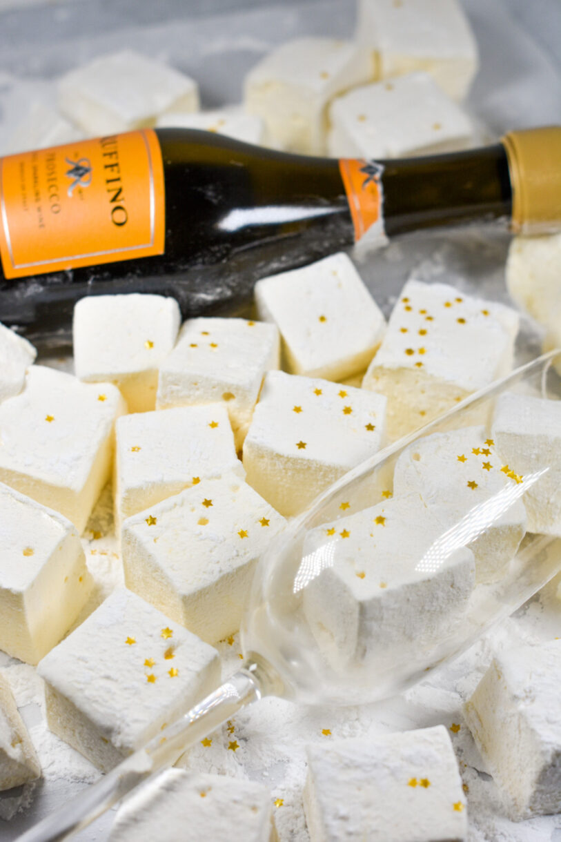 Champagne glass with homemade marshmallows and a bottle of prosecco on a white surface