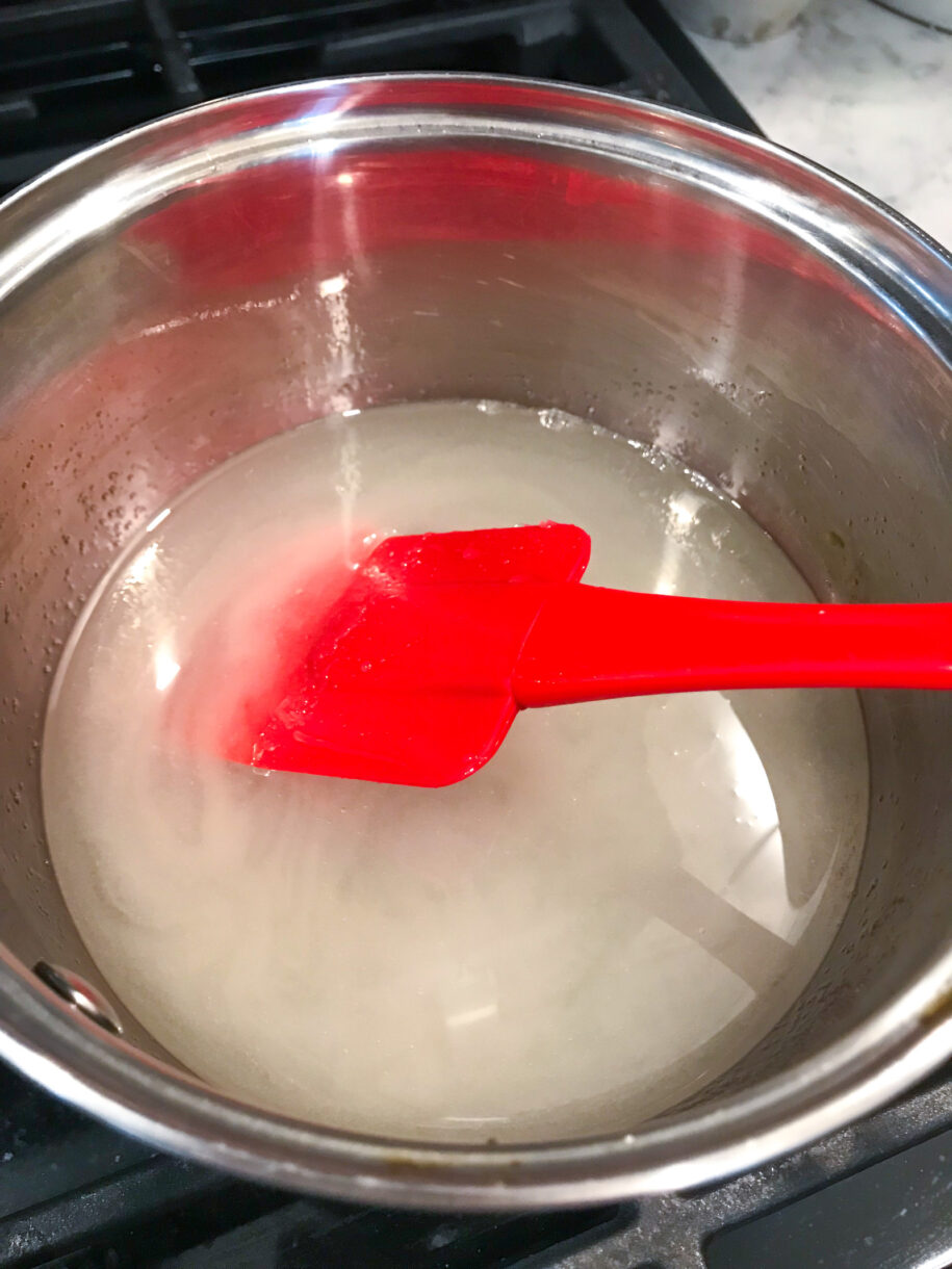 A saucepan with sugar, water, and a red spatula