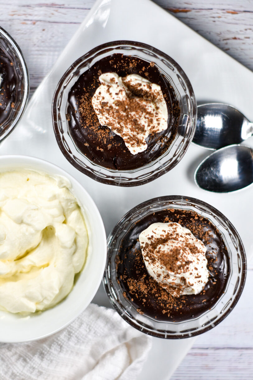 Bowls of chocolate pudding on a white tray, along with a dish of whipped cream and a white tea towel