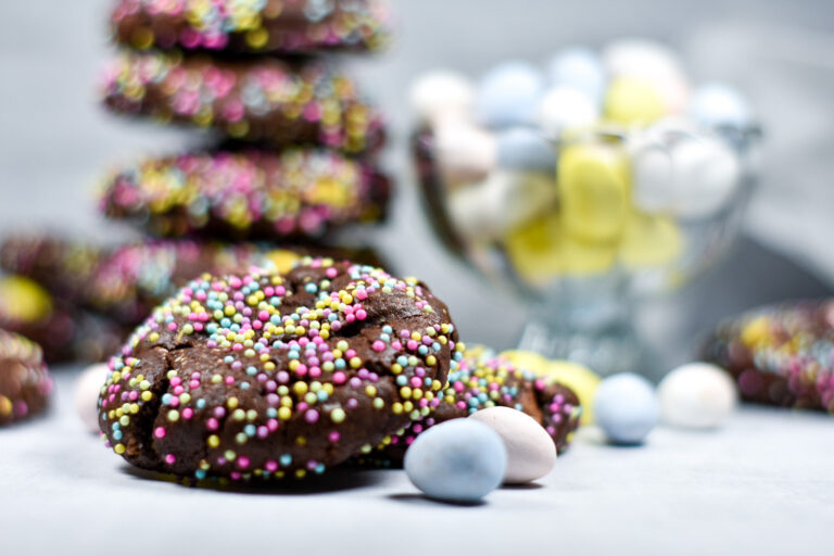 Chocolate Cadbury mini egg cookies coated in pastel nonpareils, with a bowl of mini eggs nearby