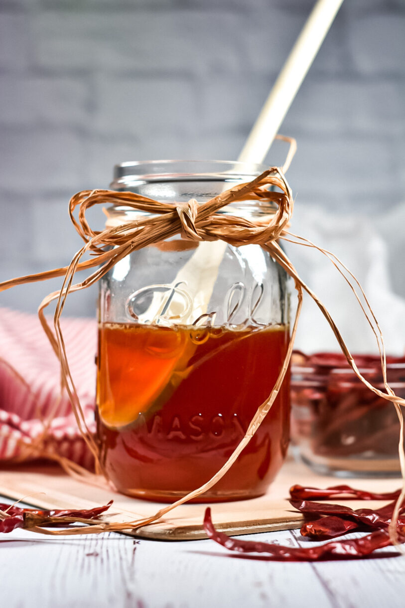 Hot honey in a glass canning jar decorated with a twine bow, and a wooden spoon 