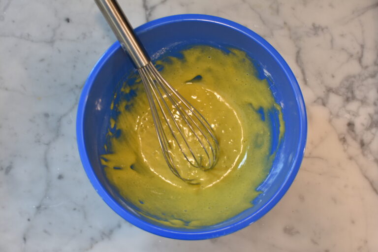 Pastry cream ingredients whisked together, in a blue bowl with a metal whisk