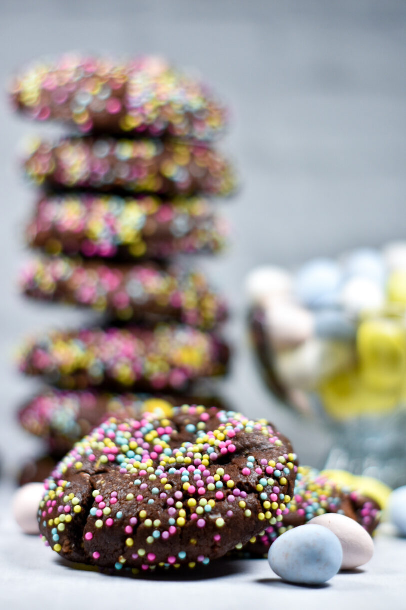 Chocolate Cadbury mini egg cookies coated in pastel nonpareils, with a bowl of mini eggs nearby