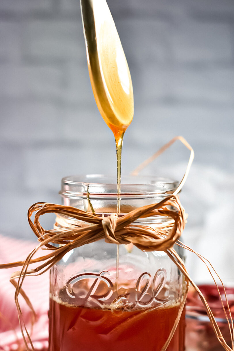 A wooden spoon drizzling honey into a canning jar