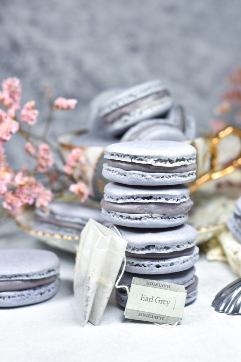 A stack of Earl Grey macarons, a tea bag, and pink flowers