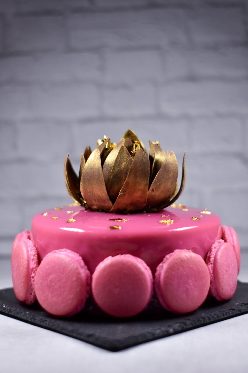 Macarons and chocolate rose adorning a pink passionfruit, coffee, and chocolate entremet