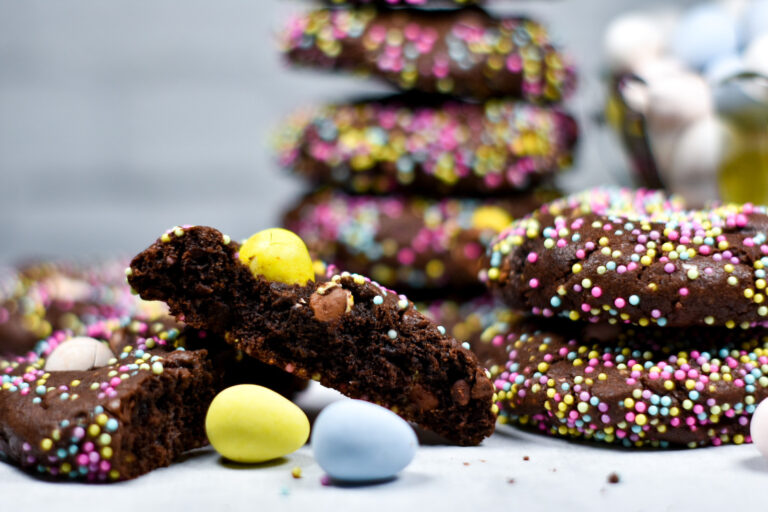A sliced chocolate Easter cookie with a pair of cookies next to it, and mini eggs scattered around